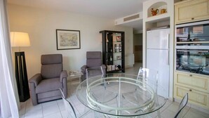 A modern living room with a glass coffee table, two armchairs, a bookshelf, and a kitchen area with a refrigerator. - Bright cocoon with terrace and sea view (Saint-Raphaël)