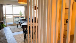 A room with a large window, a dining table with chairs, a sofa, and a hanging light fixture. - Aux Flots Bleus,  avec balcon et vue sur mer (Trouville-sur-Mer)
