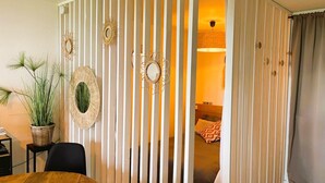 A room with a wooden dining table, a potted plant, and a decorative wall panel with vertical slats and circular mirrors. - Aux Flots Bleus,  avec balcon et vue sur mer (Trouville-sur-Mer)