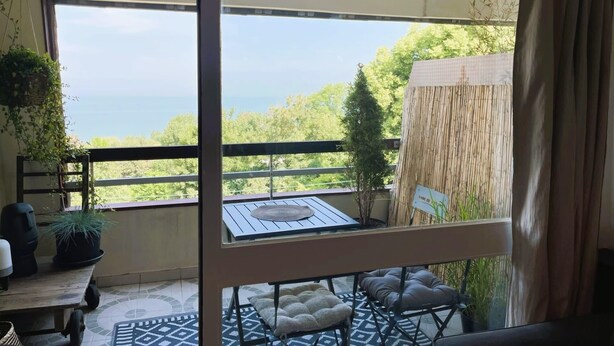 A balcony with a table and chairs, a hanging plant, and a view of the sea. - Aux Flots Bleus,  avec balcon et vue sur mer (Trouville-sur-Mer)