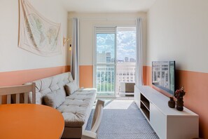 Quarto de hotel com sofá, mesa, televisão e vista para a cidade pela janela.