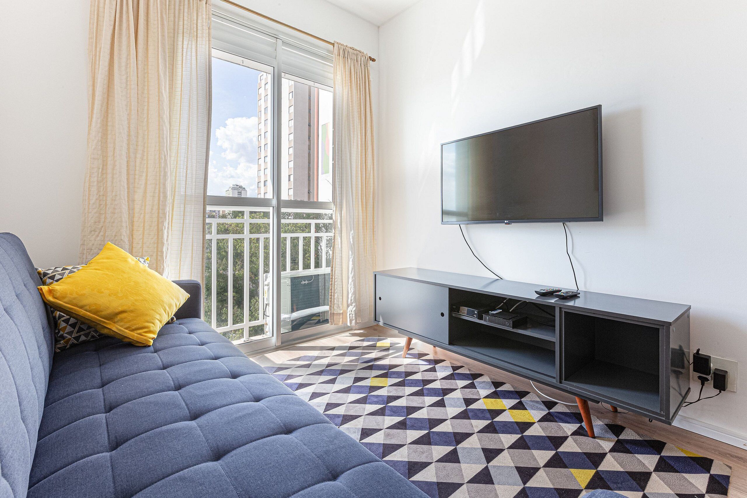 A modern living room with a sofa, a flat-screen TV mounted on the wall, and a patterned floor.