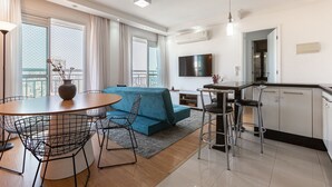 A modern hotel room with a sofa, dining table, chairs, kitchen area, and a TV. - Vossa Bossa Pinheiros (São Paulo)