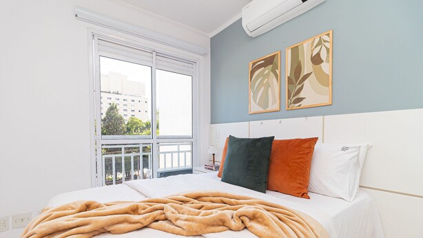 A bedroom with a large bed, a window with a view of buildings, and two wall art pieces. - Vossa Bossa Pinheiros (São Paulo)