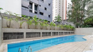 A swimming pool with a tiled deck, surrounded by a brick wall and greenery. - Vossa Bossa Pinheiros (São Paulo)