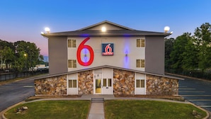 A modern building with a large '6' sign, stone facade, and a parking lot.