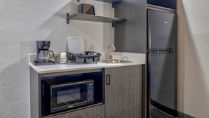 A compact kitchen with a built-in microwave, a coffee maker, and a stainless steel refrigerator.
