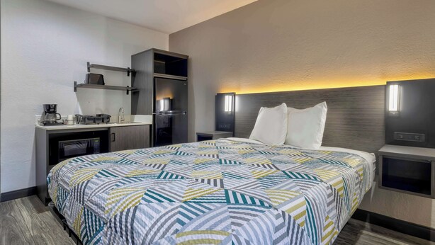 A hotel room with a large bed, a desk with a coffee maker, a microwave, and a TV.