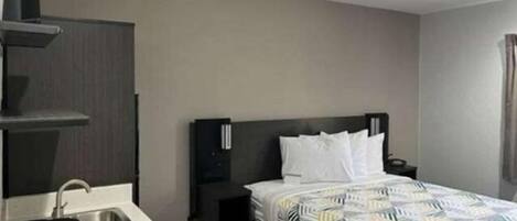 A hotel room with a bed, a nightstand, a coffee maker, and a small table.