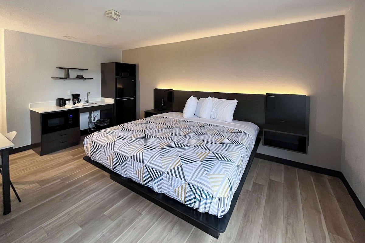 A modern hotel room with a large bed, a desk with a sink, a microwave, and a refrigerator.