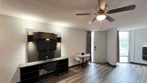 A modern living room with a flat-screen TV mounted on the wall, a dining table with chairs, and a ceiling fan. - Studio 6 Nacogdoches, Tx – Sfa University (Nacogdoches)
