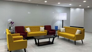 A modern waiting area with yellow sofas, red chairs, and a black coffee table. - Studio 6 Nacogdoches, Tx – Sfa University (Nacogdoches)