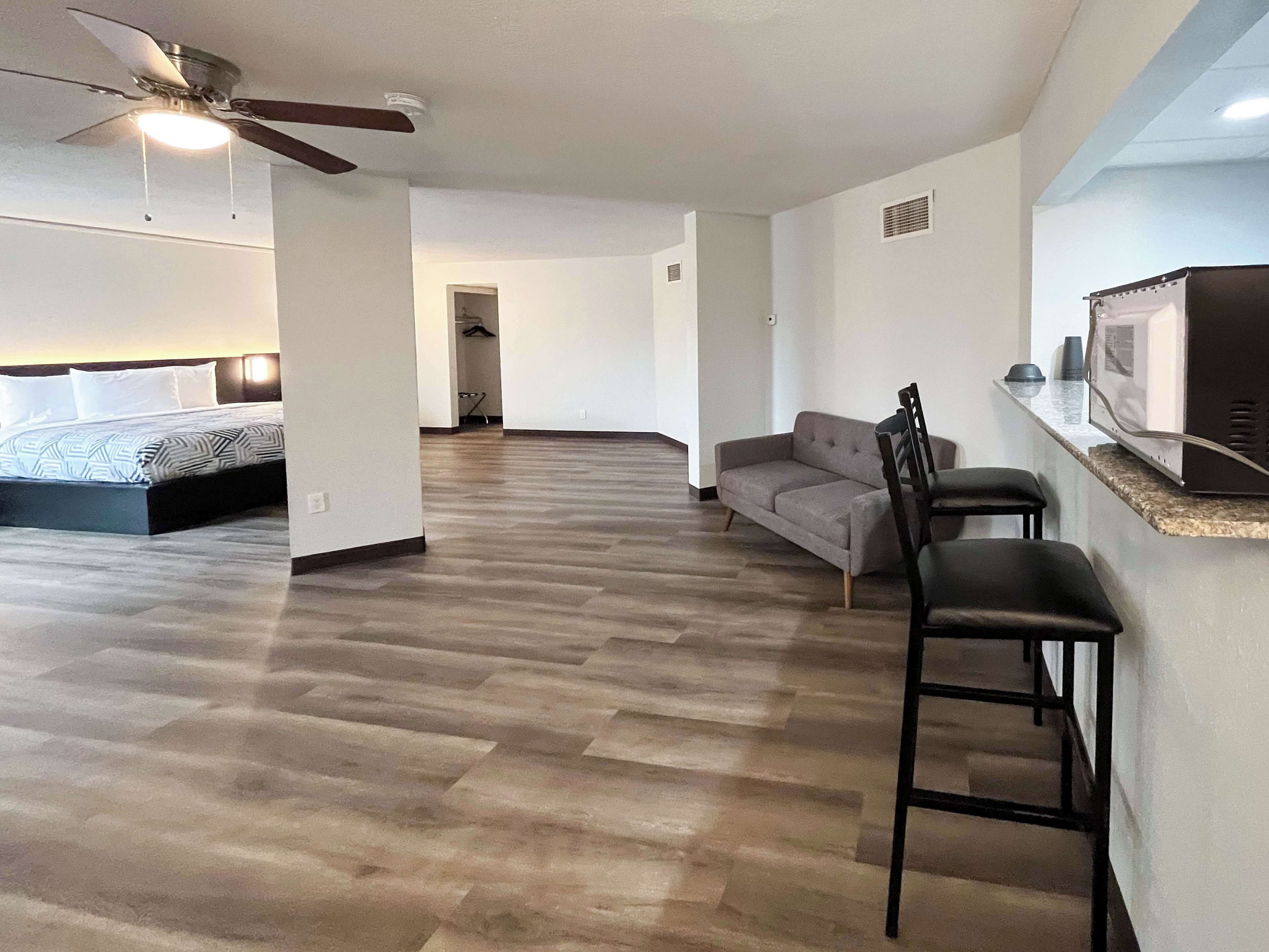 A modern living room with a bed, a gray sofa, and a kitchen area with a microwave.