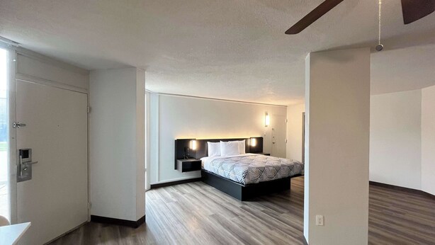 A modern hotel room with a large bed, a bedside table, a nightstand, and a wall-mounted light. - Studio 6 Nacogdoches, Tx – Sfa University (Nacogdoches)