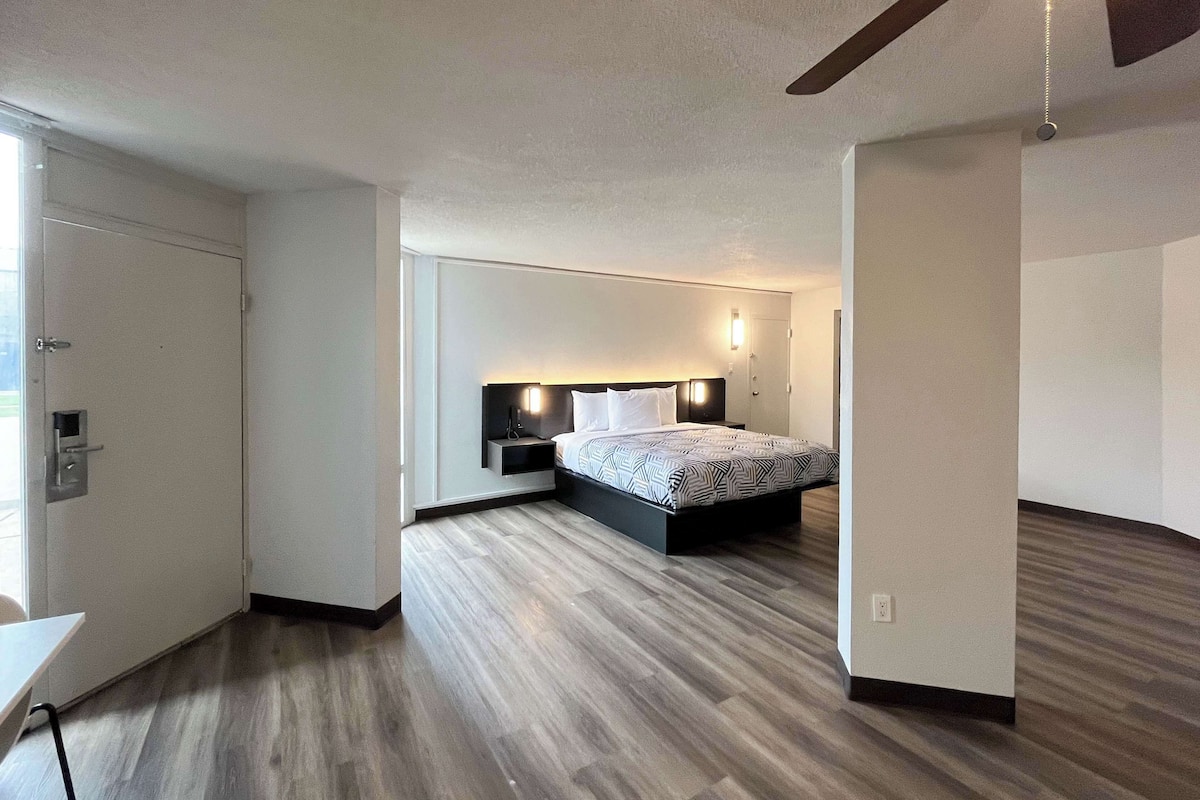 A modern hotel room with a large bed, a bedside table, a nightstand, and a wall-mounted light.
