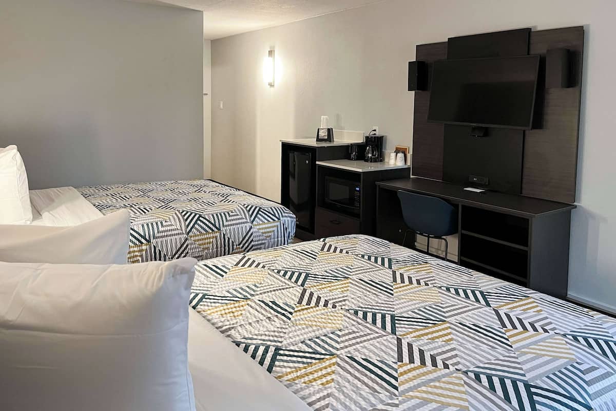 A hotel room with two beds, a desk, a chair, a TV, and a coffee maker.