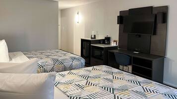 A hotel room with two beds, a desk, a chair, a TV, and a coffee maker.