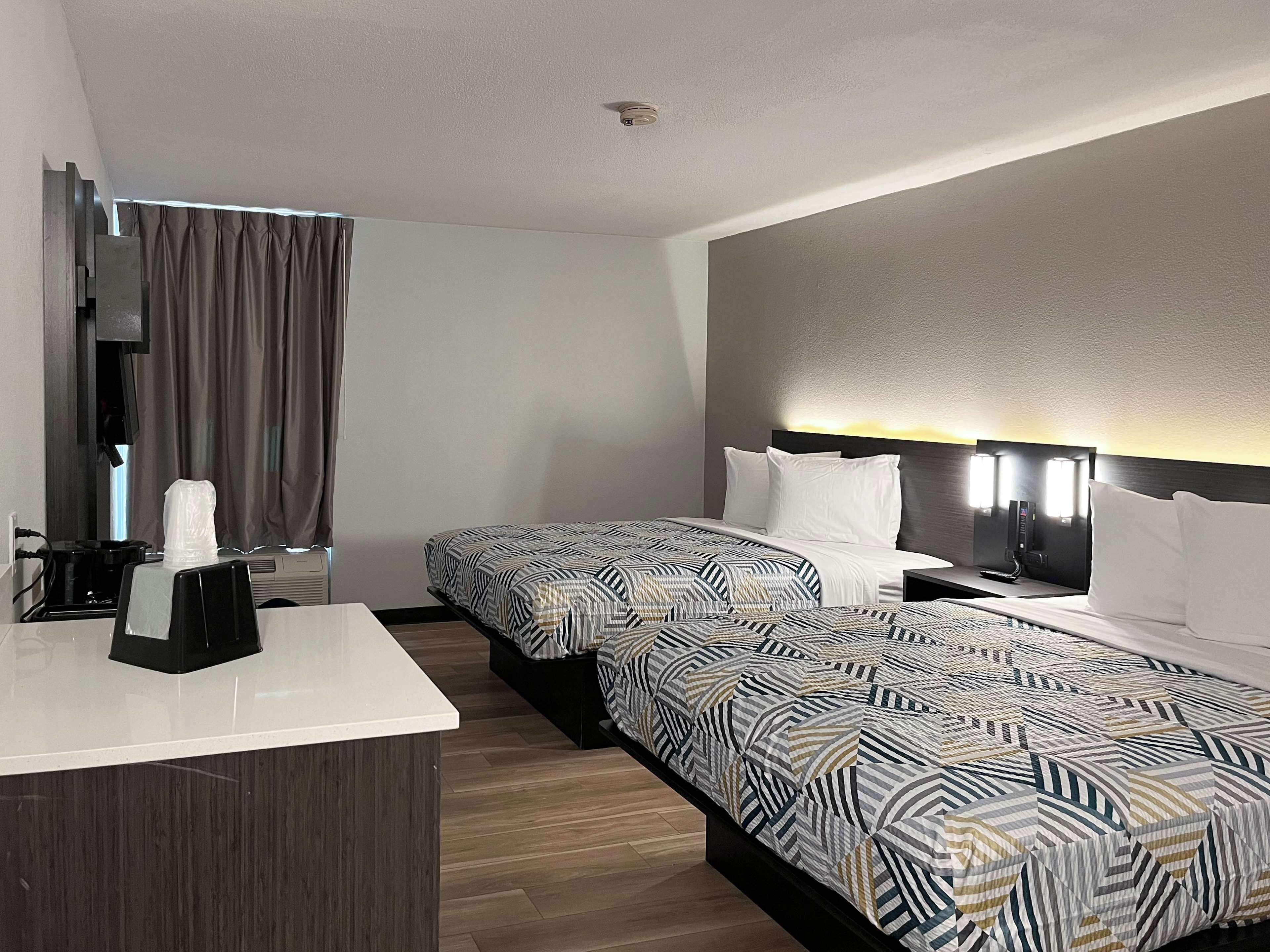 Une chambre d’hôtel avec deux lits, un bureau, une machine à café et une fenêtre avec des rideaux.