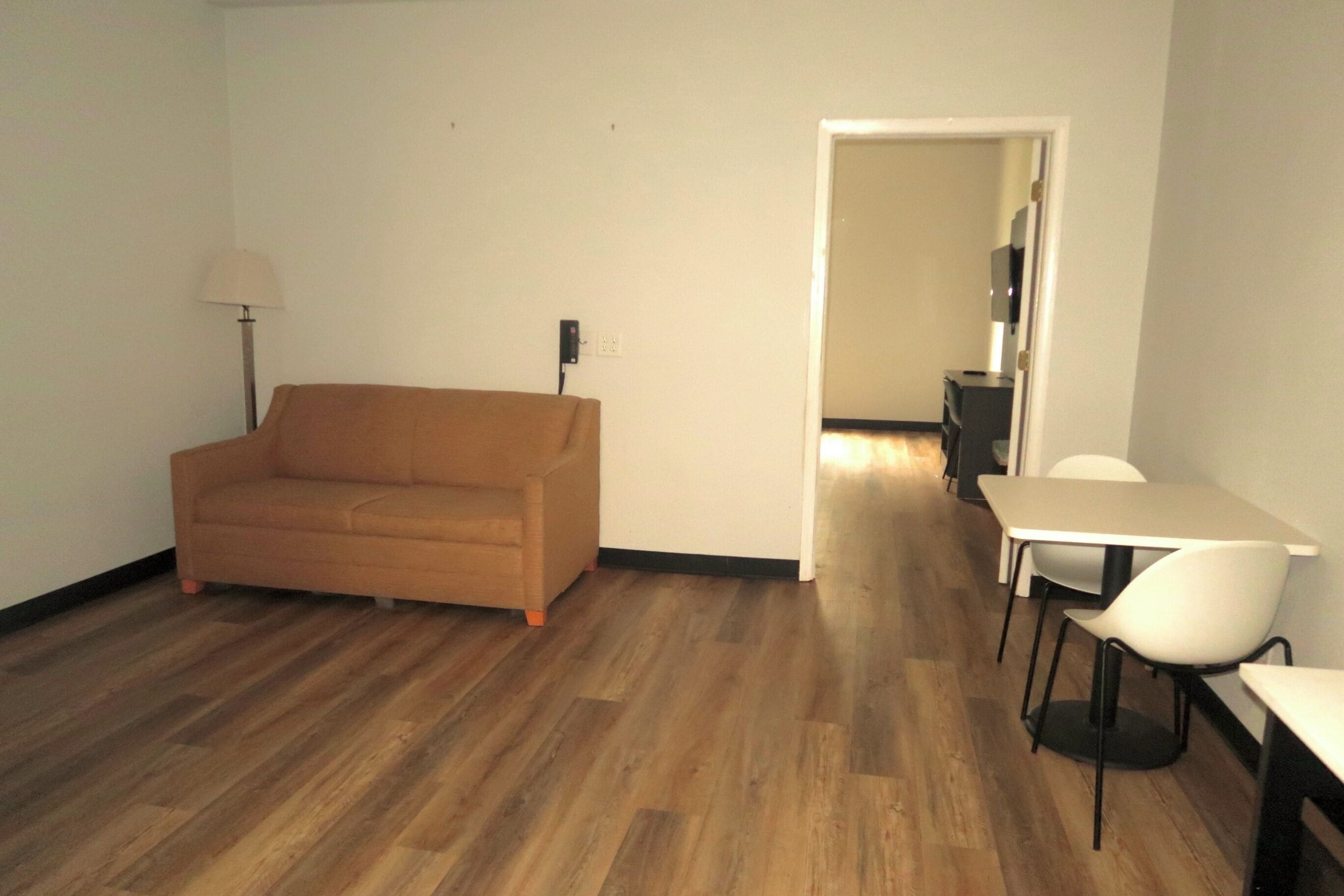 A room with a wooden floor, a sofa, a dining table with chairs, and a lamp.