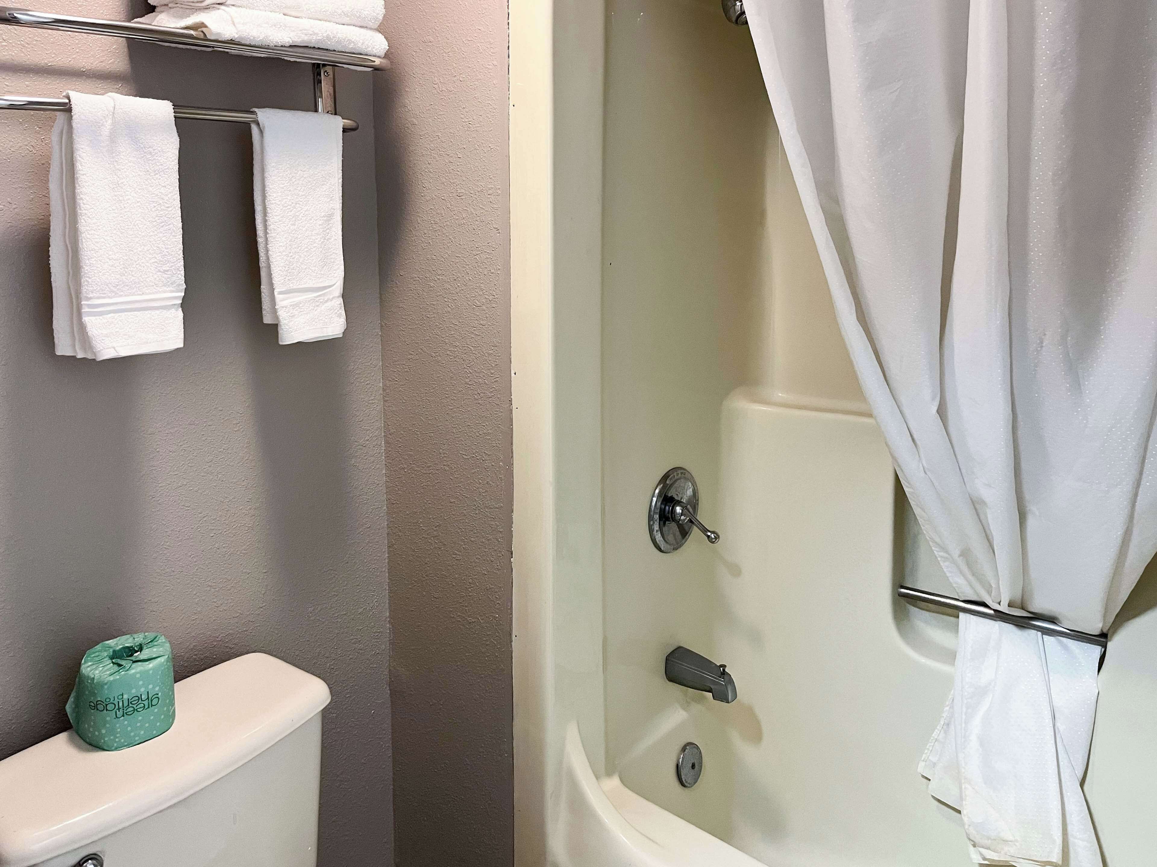 A bathroom with a toilet, a bathtub with a shower curtain, and a towel rack with several towels.