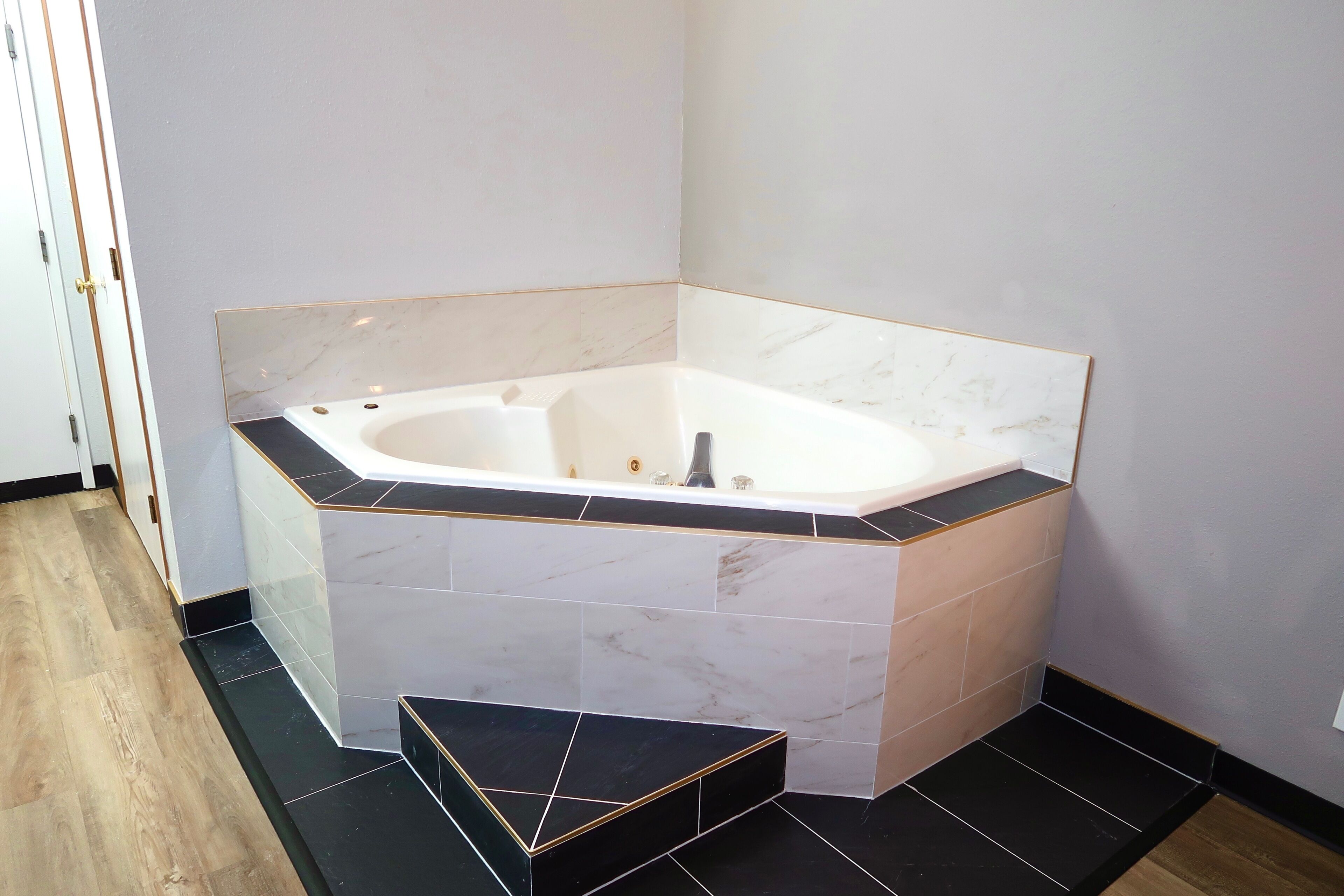 Une salle de bain d’angle avec une baignoire sur pieds, des murs carrelés et un plancher en bois.