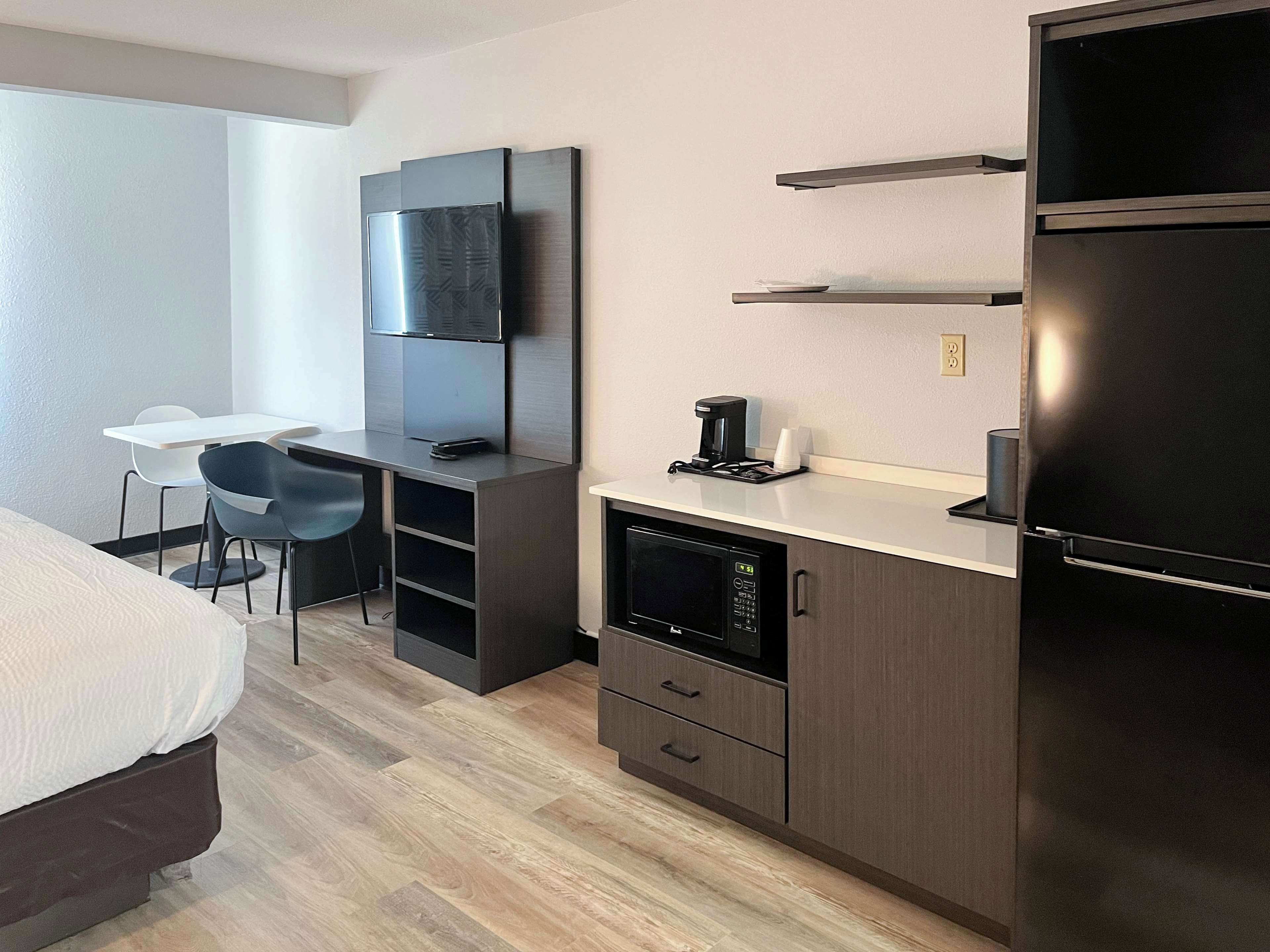 A modern hotel room with a bed, a desk with a chair, a flat-screen TV, a coffee maker, and a built-in microwave.