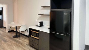 Cozinha compacta com geladeira preta, bancada branca, cafeteira e pequena mesa de jantar com cadeiras.