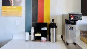 Cozinha com máquina de café, bebedouro de aço inoxidável e painel de azulejos coloridos.