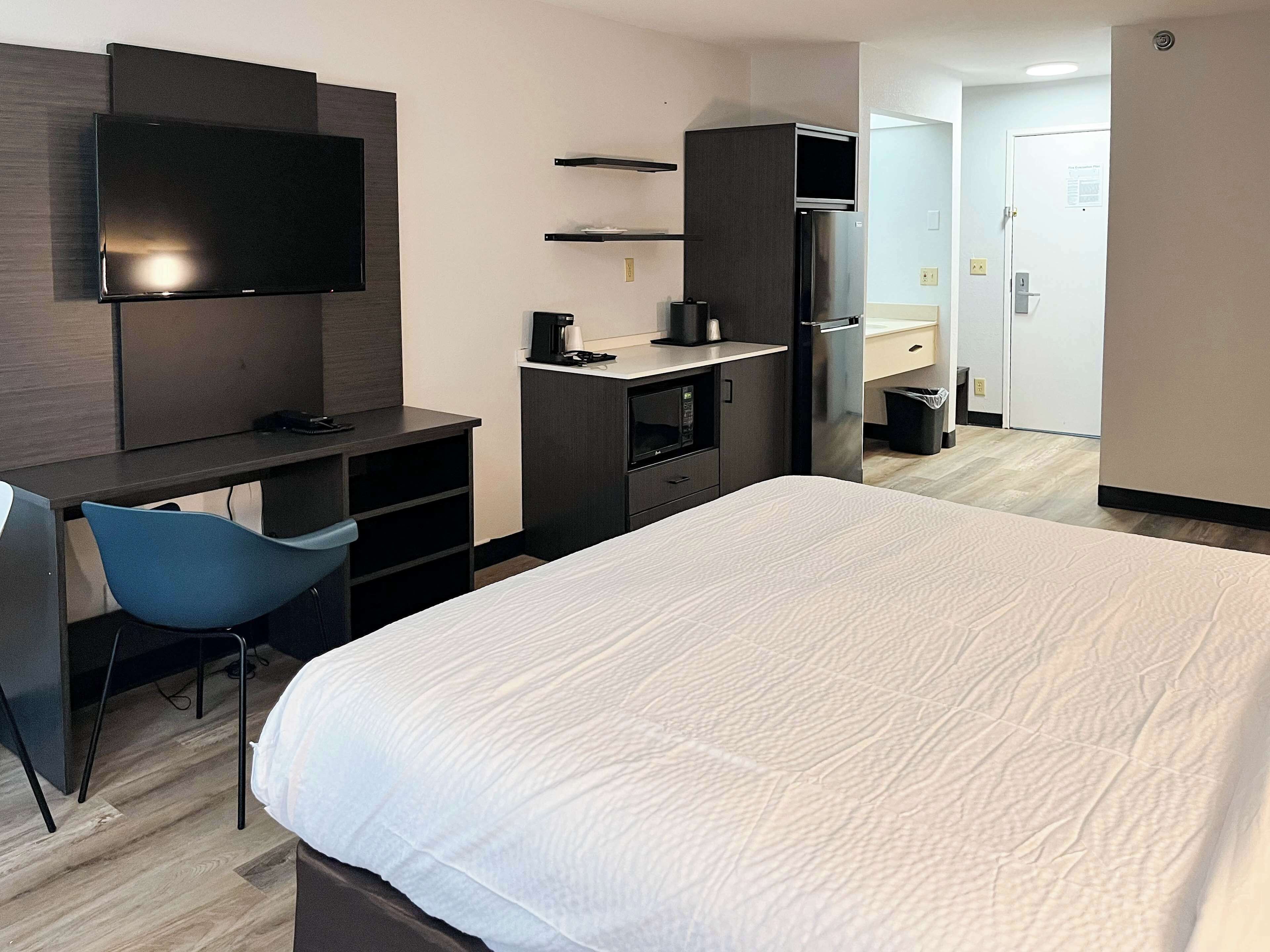 A hotel room with a bed, a desk, a chair, a TV, a microwave, a refrigerator, and a trash bin.