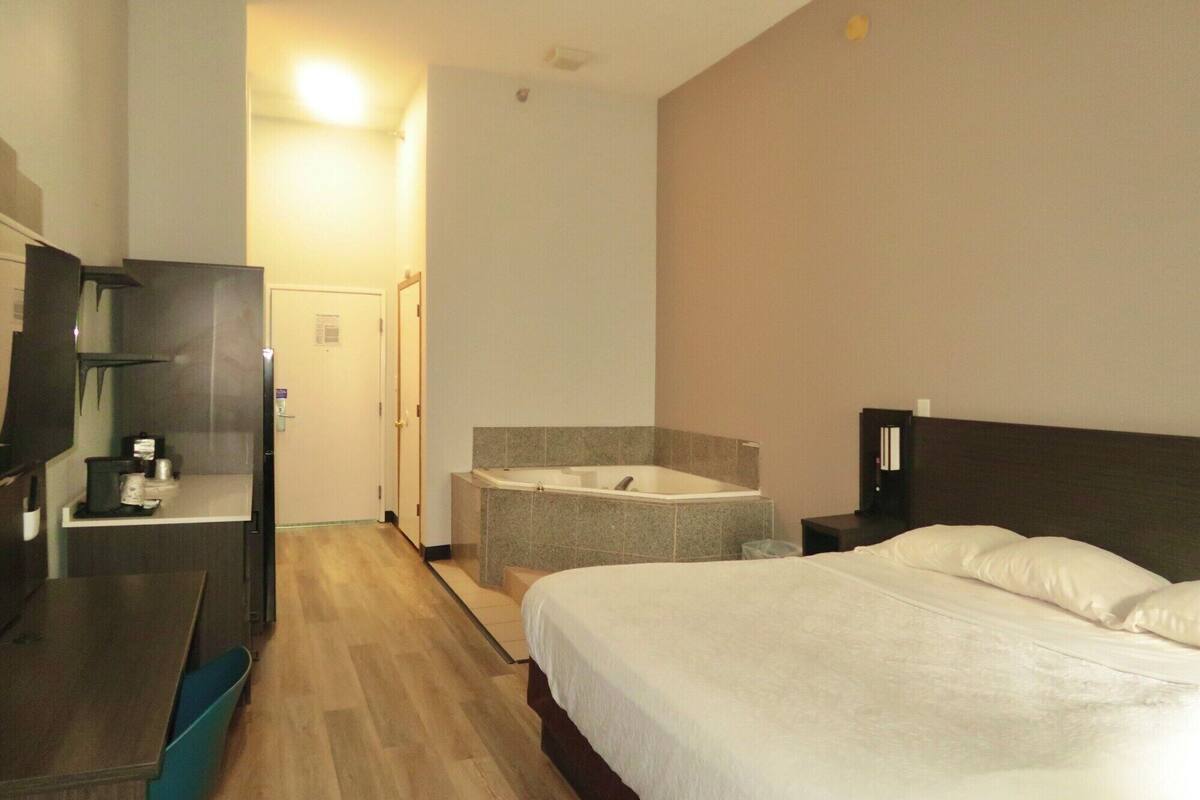 A hotel room with a bed, a small sitting area with a chair, a desk, and a bathtub.