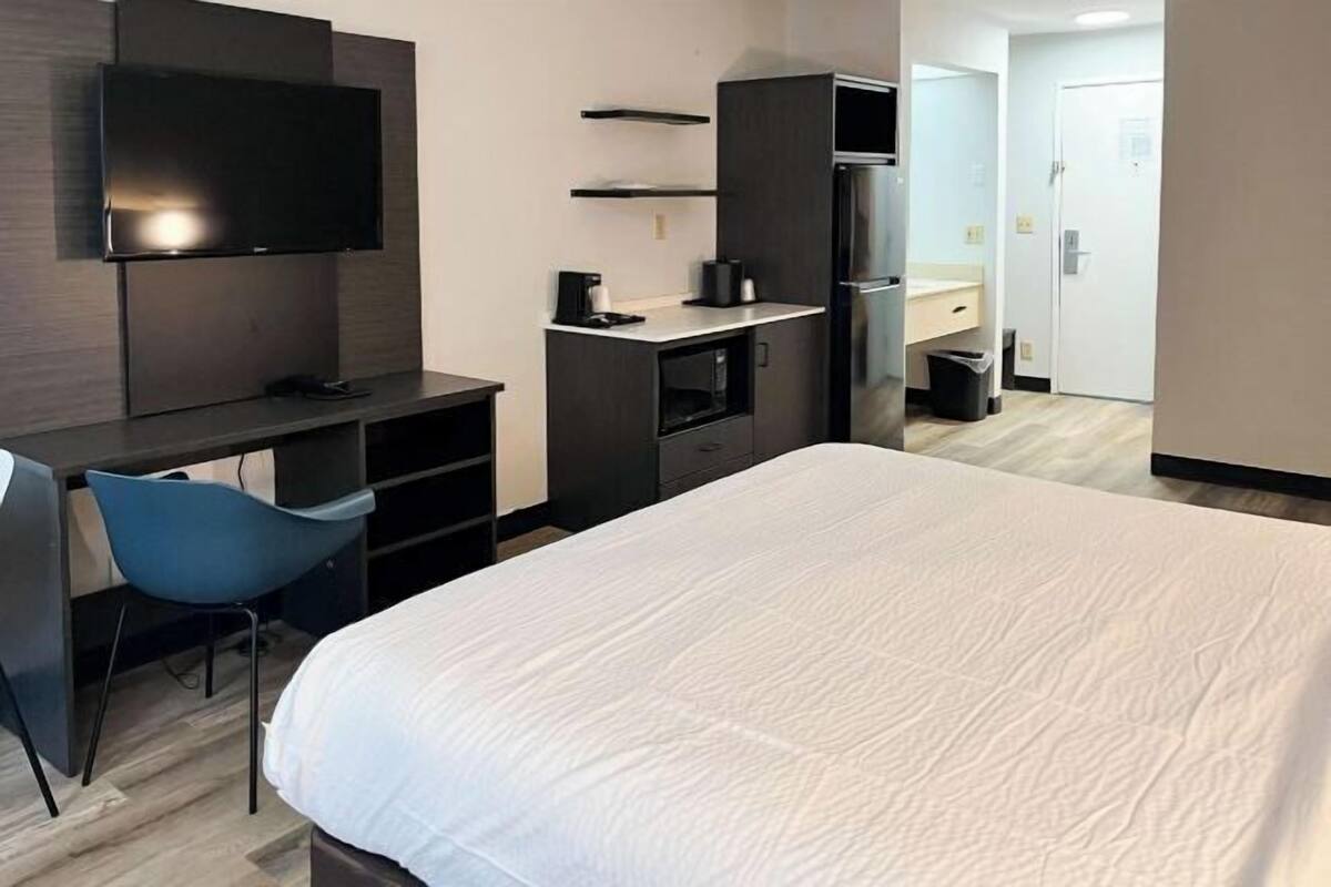 A hotel room with a bed, a desk with a chair, a television mounted on the wall, a wardrobe, and a door leading to a bathroom.