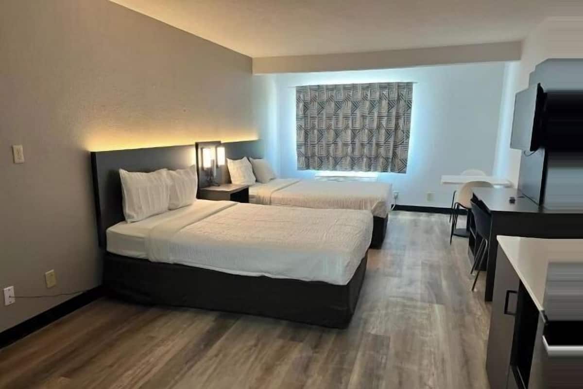 A hotel room with two beds, a desk, and a television.