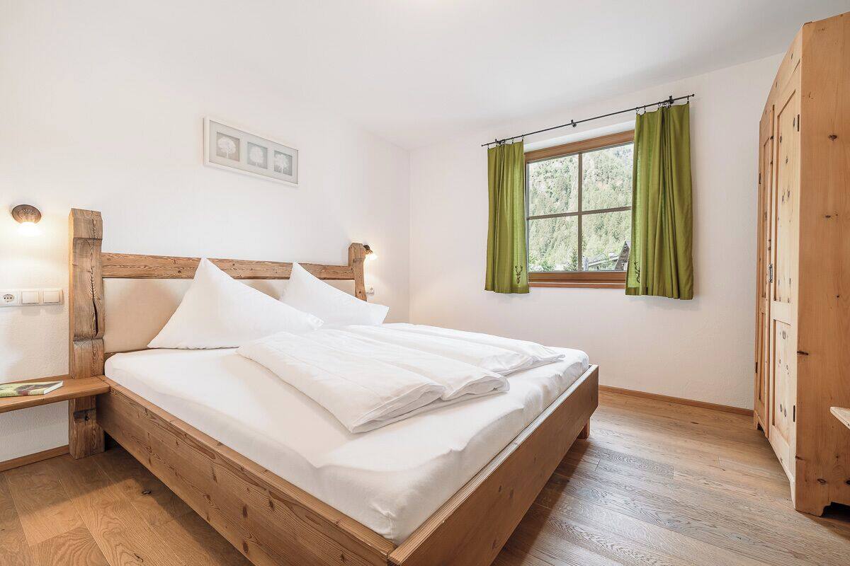 A wooden bed in a room with a window, a nightstand, and a wardrobe.