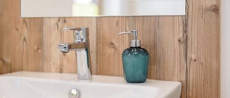 Ein Badezimmer mit einem weißen Waschbecken, einem Wasserhahn und einem türkisfarbenen Seifenspender.