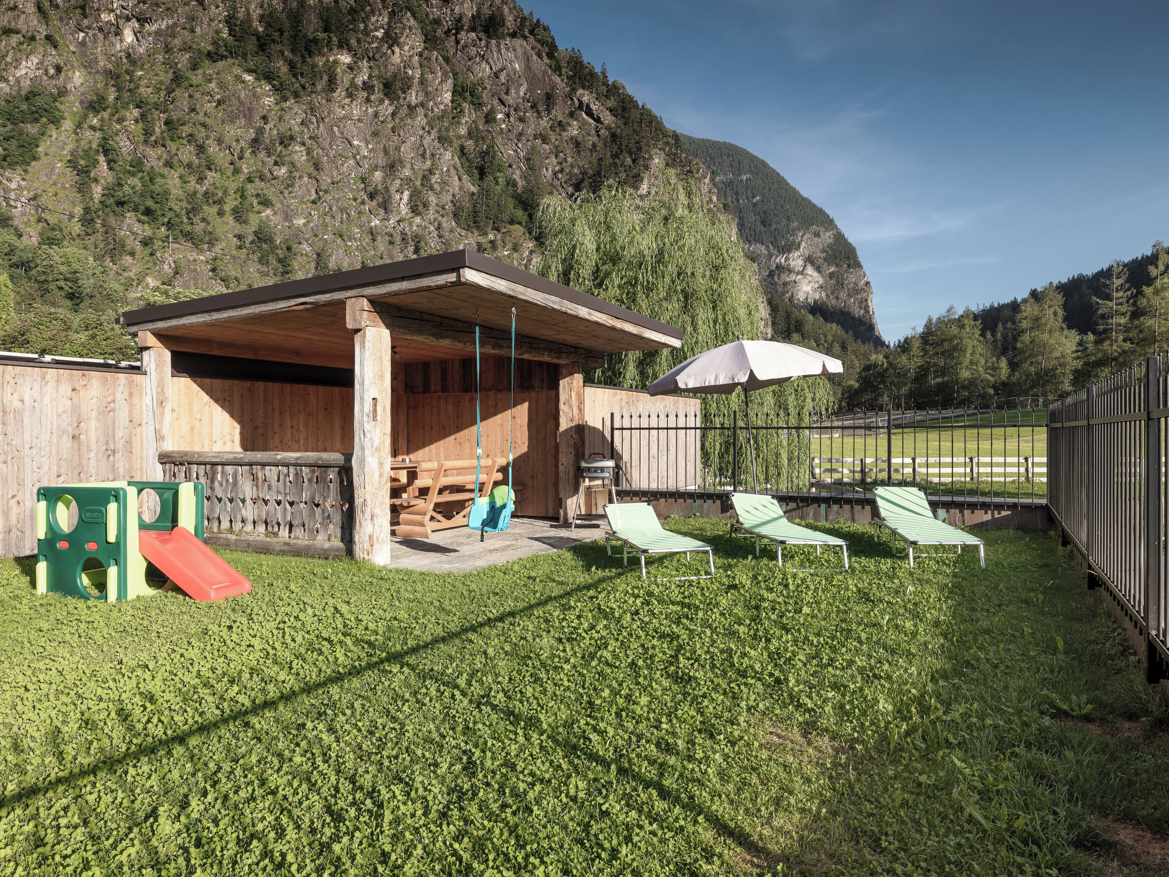 Een houten zitgedeelte buiten, met een overdekte patio, een glijbaan en uitzicht op een bergachtig landschap.
