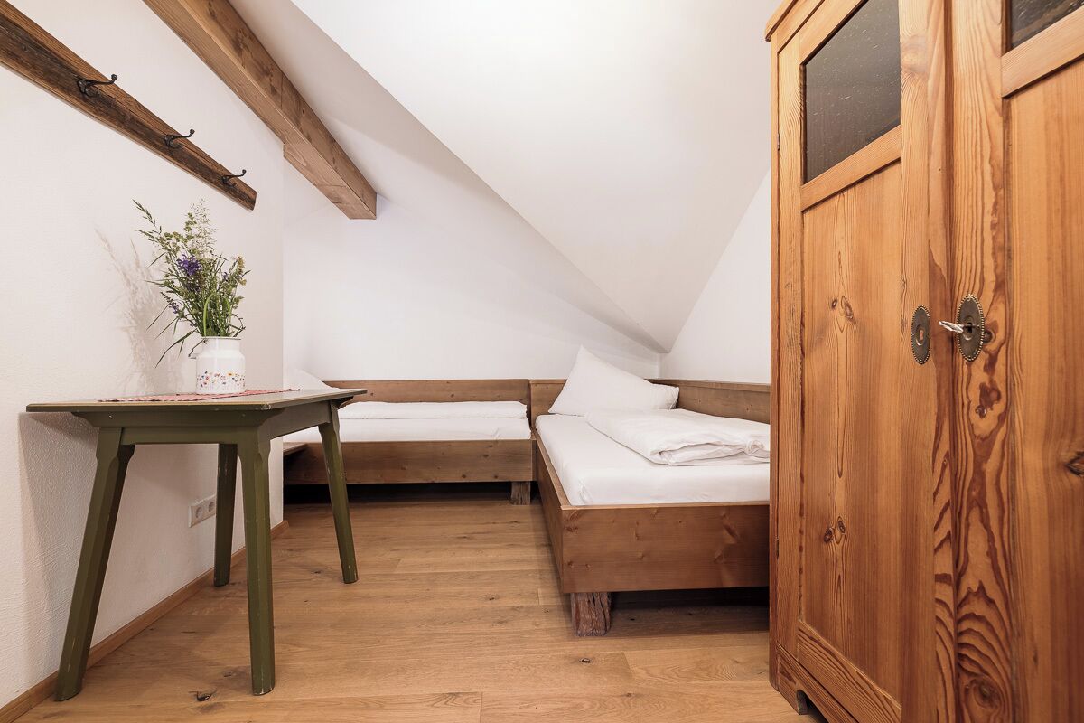 Una stanza accogliente e piccola, con un letto di legno, un armadio di legno e un tavolino con un vaso di fiori.