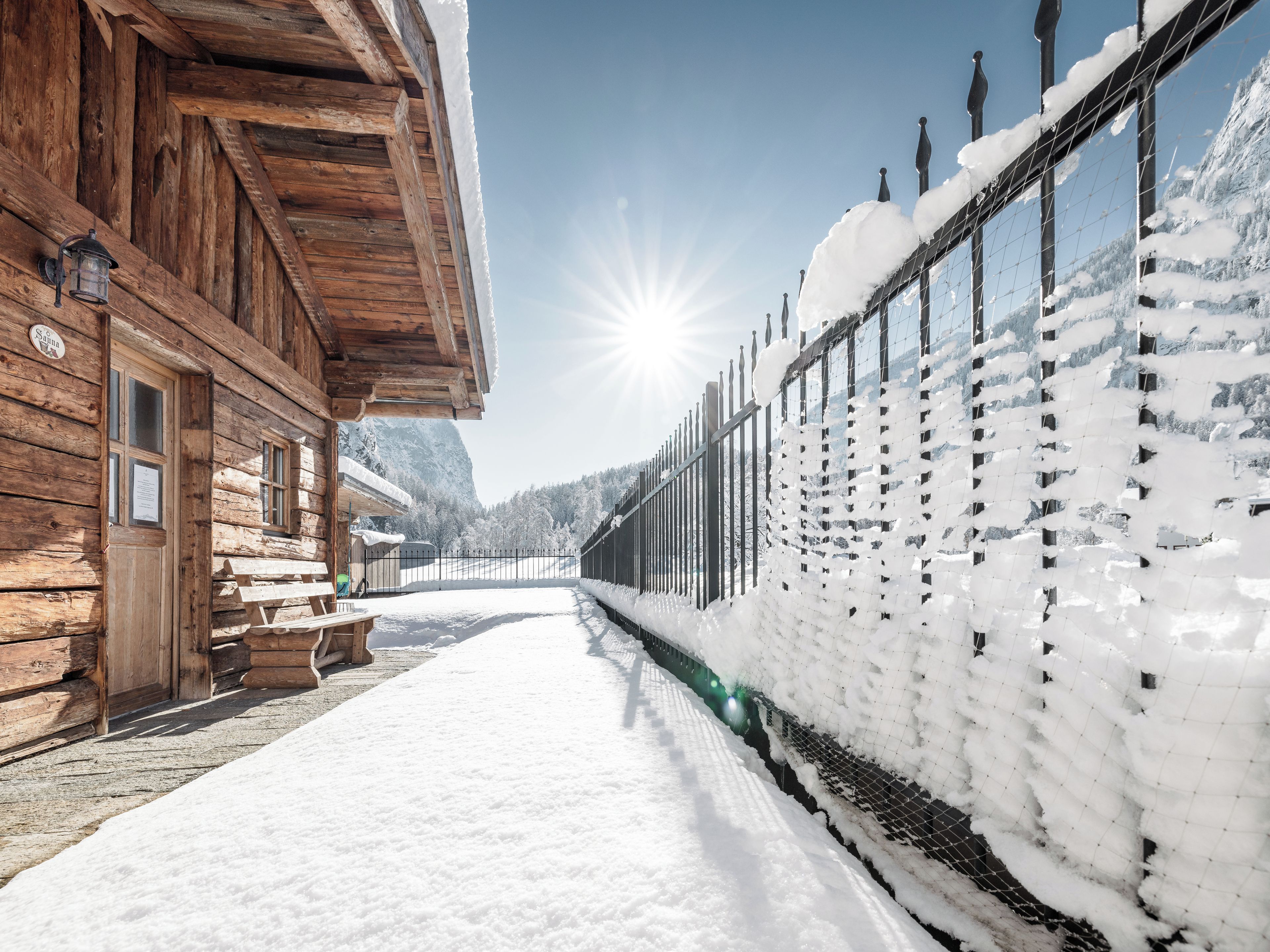 Un edificio in legno con una panchina e un segnale, un sentiero coperto di neve e una recinzione con accumuli di neve.