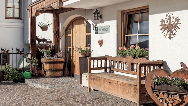 A traditional building with a wooden bench, a heart-shaped planter with flowers, a wooden sign, and a deer decoration. - MYALPS Mühlhof (Oetz)