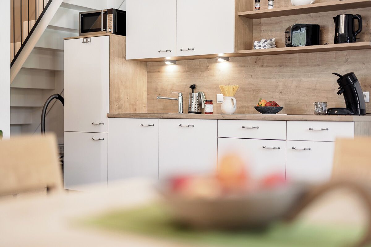 Een moderne keuken met witte kastjes, een houten aanrechtblad en een inbouwmagnetron.
