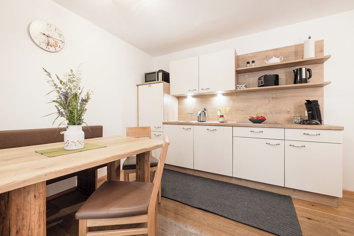 Una cocina moderna con armarios blancos, encimera de madera y un microondas. Hay una mesa de comedor con sillas y un florero con flores.