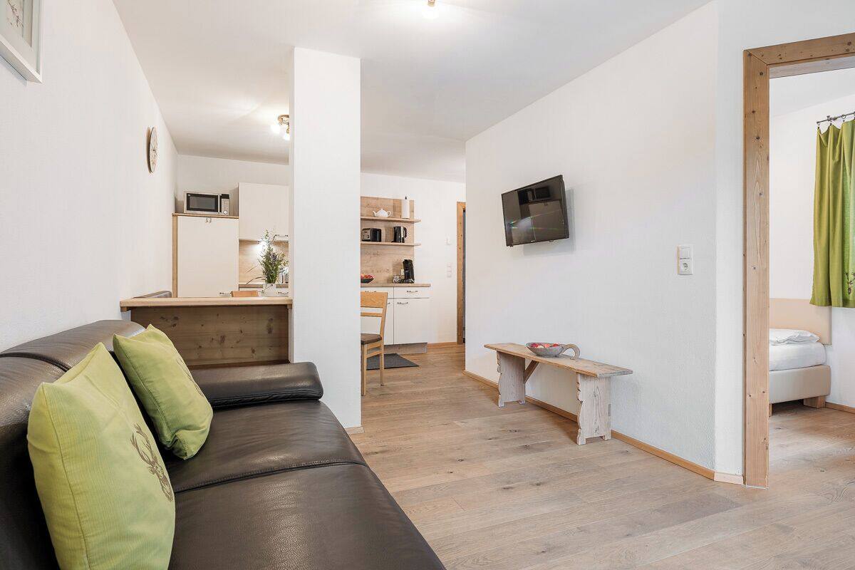 A modern living room with a black leather sofa, a small white table, and a TV mounted on the wall.