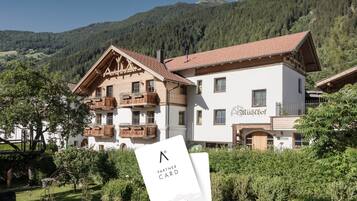 A traditional Alpine-style building with a wooden balcony, a sign reading 'MyAlps.at', and a garden in the foreground.