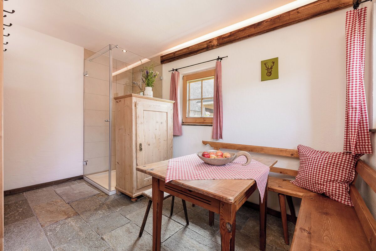 A cozy room with a wooden table, a bench, and a window with checkered curtains.