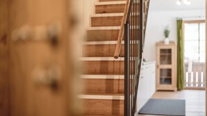 A wooden staircase with a metal railing leading to a room with a wooden floor and a door in the foreground. - MYALPS Mühlhof (Oetz)
