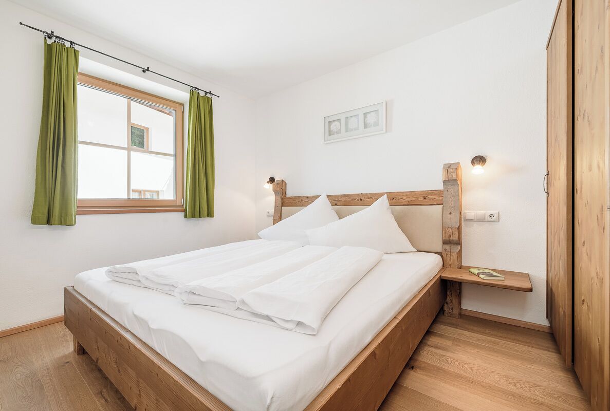 Ein ordentlich bezogenes Bett mit weißen Leinen, einem hölzernen Kopfteil und einem Nachttisch mit Lampe.