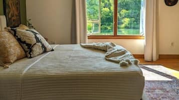 Un dormitorio con una cama grande, vistas a zonas verdes a través de una ventana, un tapete estampado y una lámpara fijada en la pared.