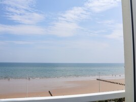 A beach view from a window, including the sea, sand, and a few people.