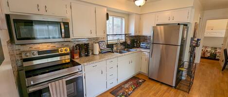 A modern kitchen with stainless steel appliances, white cabinetry, and a wooden floor.