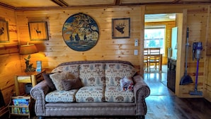 L’intérieur d’un chalet chaleureux, avec un canapé à motifs, des murs en bois, un tableau accroché et une lampe.