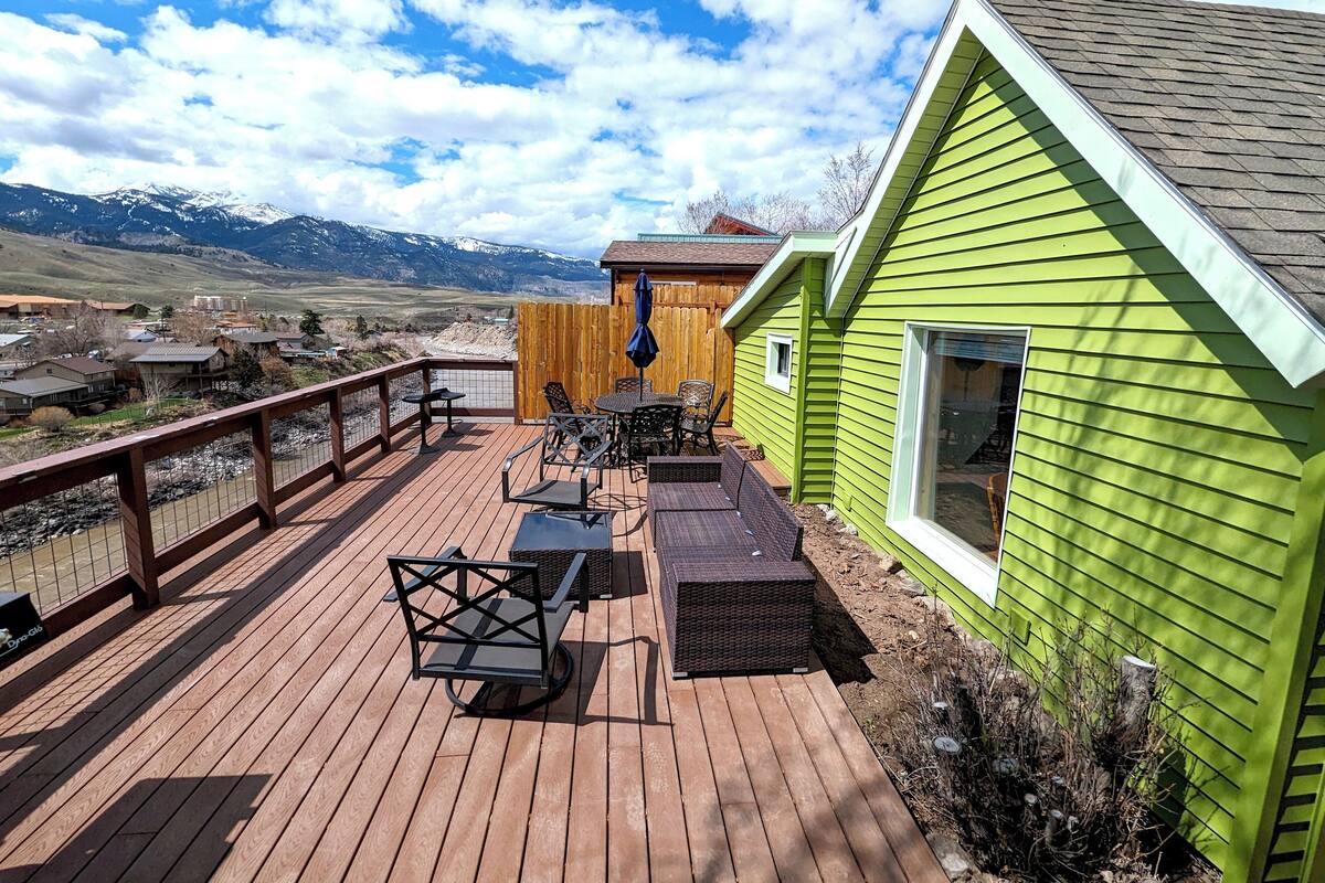 Une terrasse avec des meubles d’extérieur, une clôture en bois et un bâtiment vert doté d’une fenêtre.